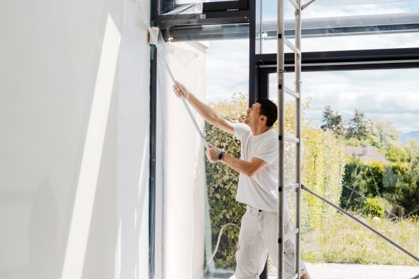 Man painting interior walls with roller in his house into white. Apartment  renovation, redecoration and repair concept.